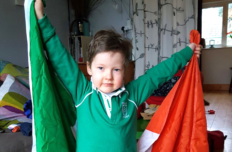 boy in green rugby top with an Ireland flag behind him