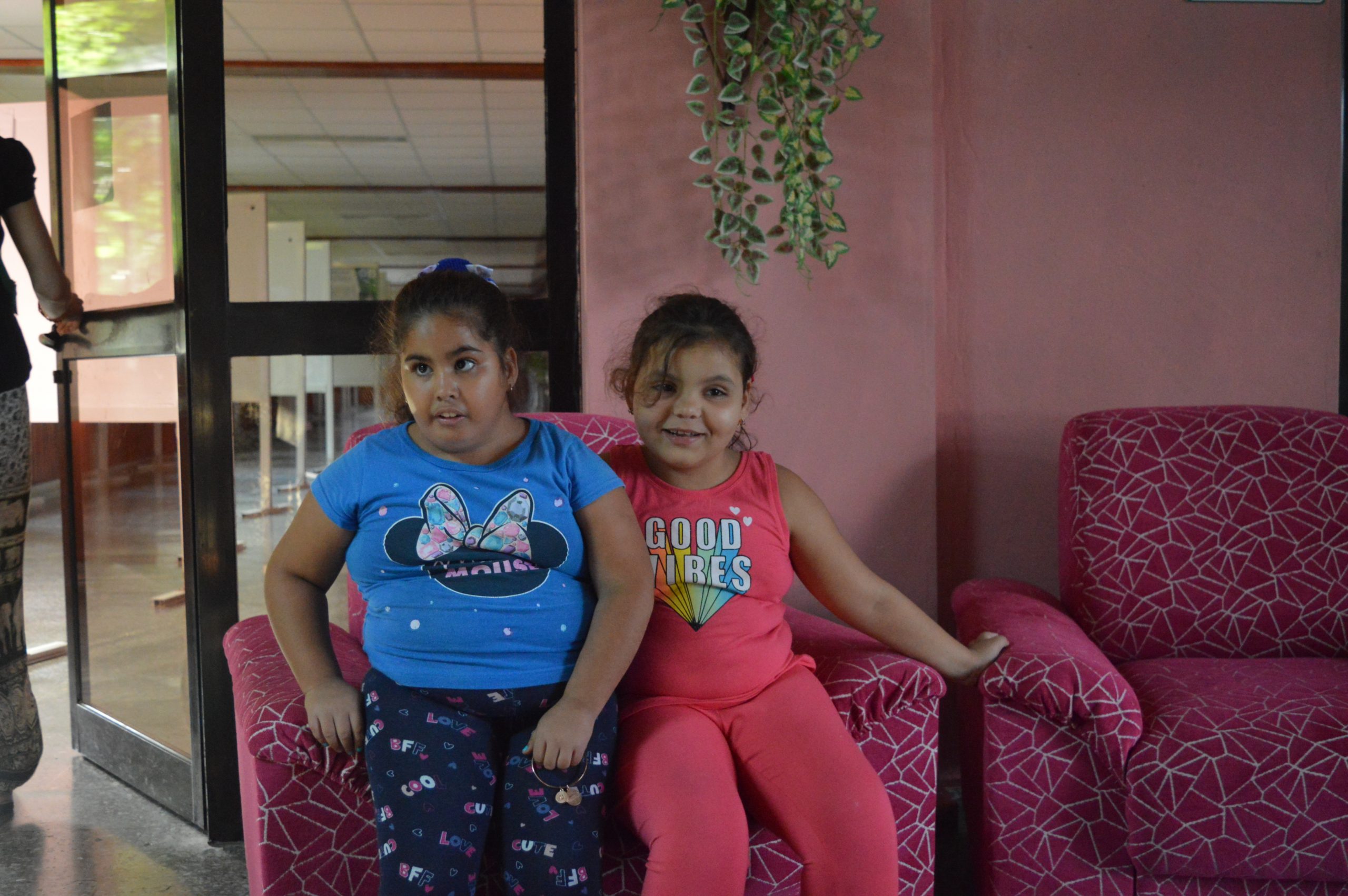 Two young girls sitting on pink sofas