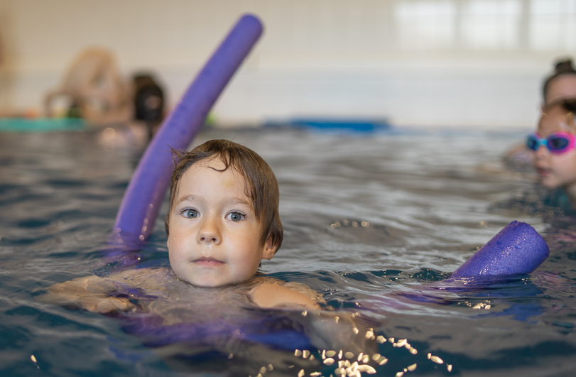 boy in swimming pool with purple swim aid