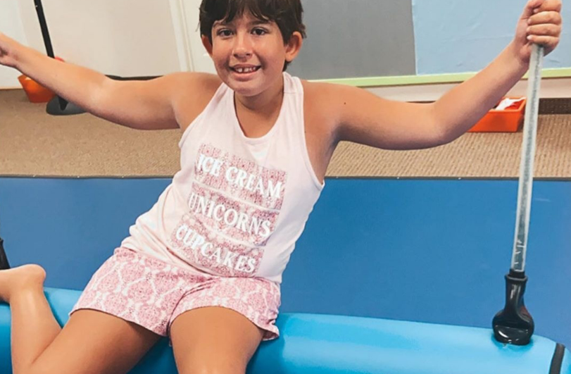 child in pale pink vest and shorts sat on gym swing