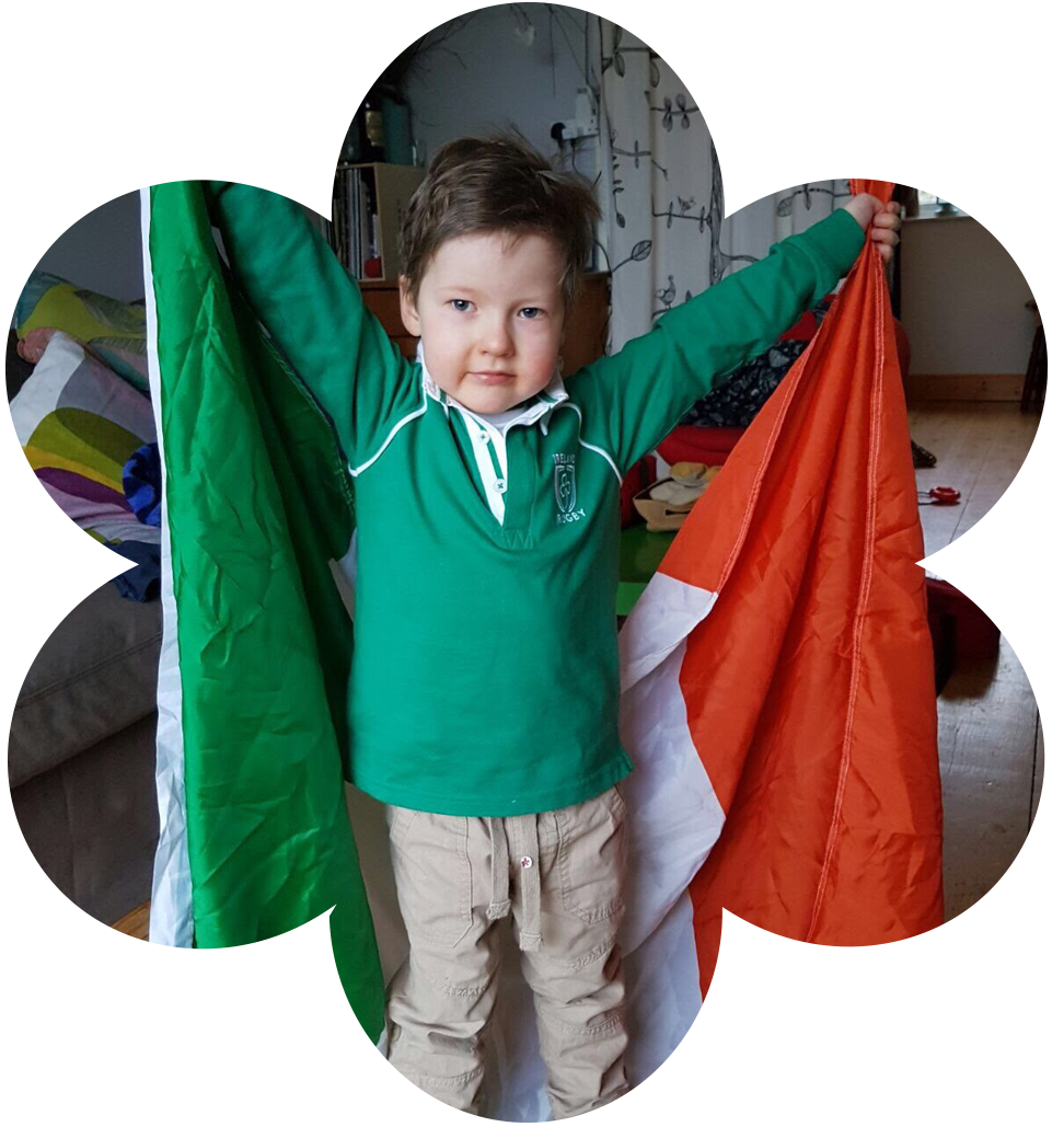 boy in green rugby top holding Ireland flag behind him