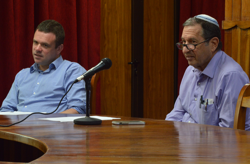 two men in blue shirts sitting at a microphone round a table